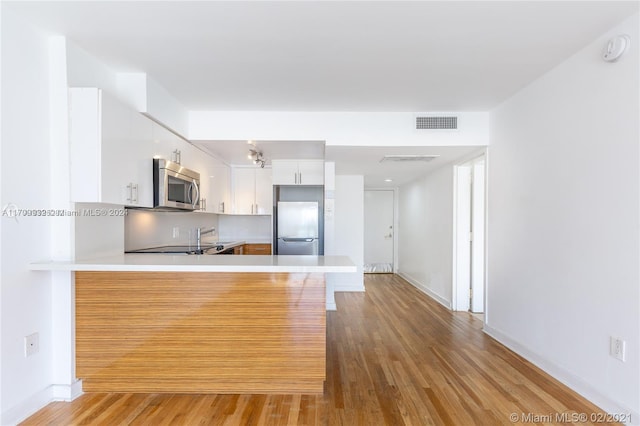 kitchen with kitchen peninsula, white cabinets, stainless steel appliances, and light wood-type flooring