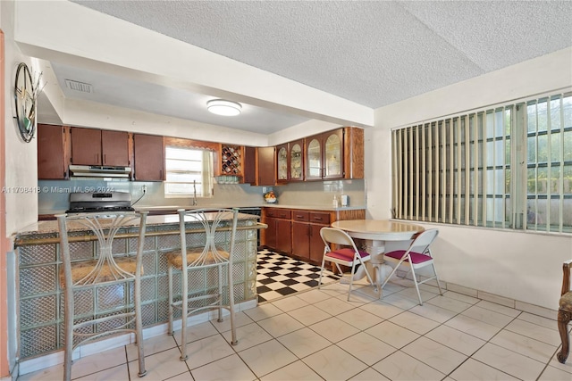 kitchen with sink, light tile patterned floors, a textured ceiling, stainless steel range oven, and kitchen peninsula