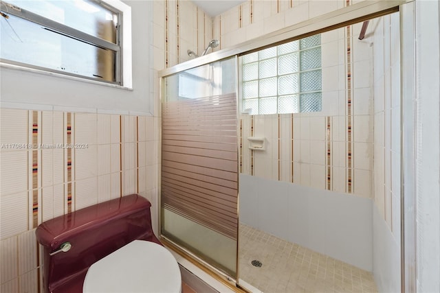 bathroom featuring toilet, plenty of natural light, a shower with shower door, and tile walls