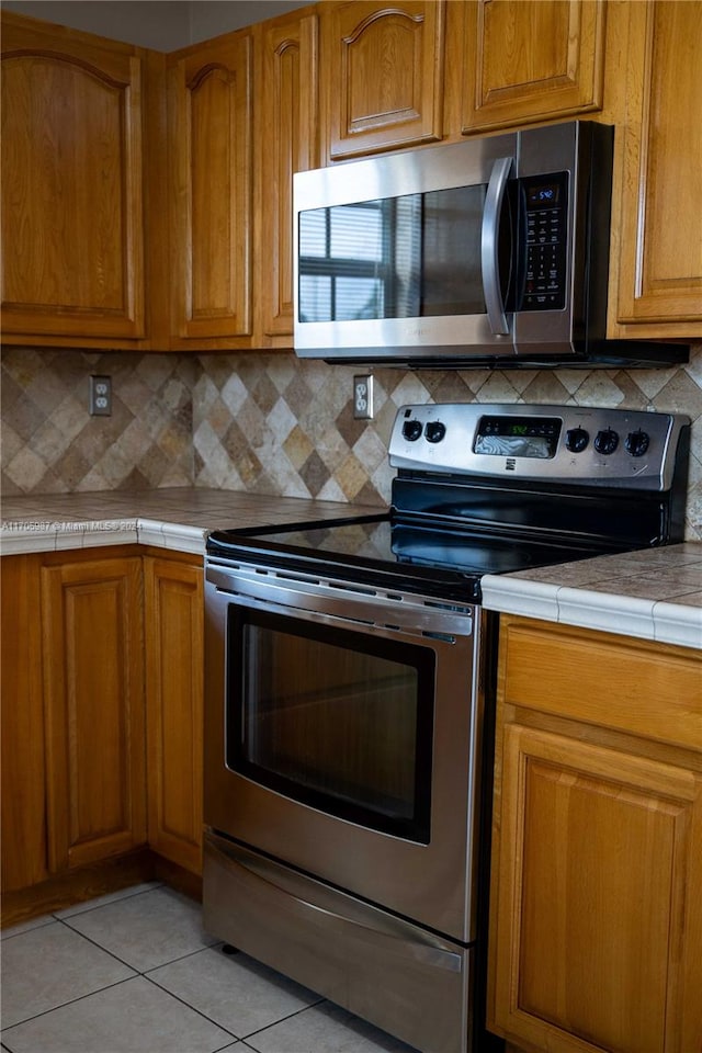 kitchen with tile countertops, light tile patterned floors, stainless steel appliances, and tasteful backsplash