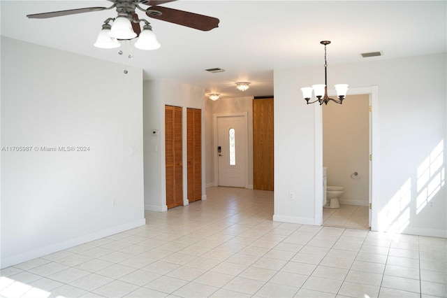 tiled spare room with ceiling fan with notable chandelier