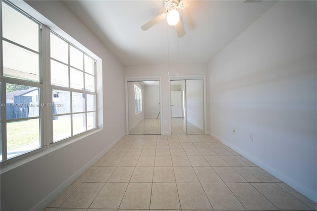 unfurnished bedroom with light tile patterned floors, ceiling fan, and multiple closets