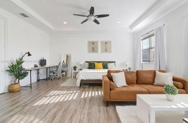 bedroom with a tray ceiling, ceiling fan, and light wood-type flooring