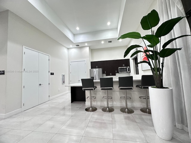 interior space with a center island, a high ceiling, a kitchen breakfast bar, light tile patterned floors, and appliances with stainless steel finishes