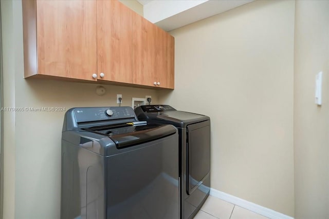 clothes washing area featuring washer and clothes dryer, cabinets, and light tile patterned floors