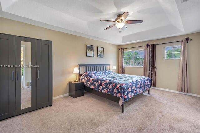 bedroom with ceiling fan, a raised ceiling, and light carpet