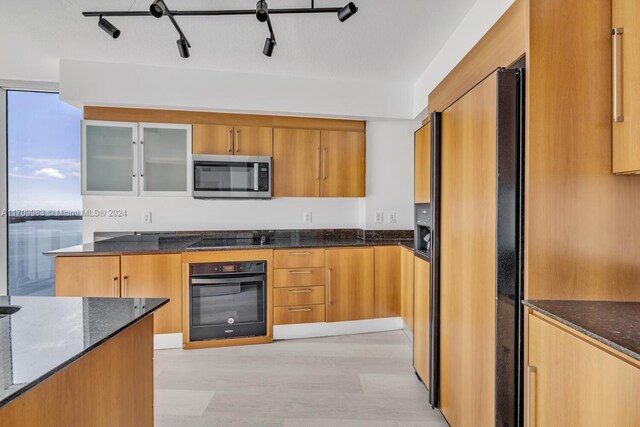 335 S Biscayne Blvd Unit 4109, Miami, FL 33131 - kitchen with glass insert cabinets, black appliances, dark stone counters, and light wood-type flooring