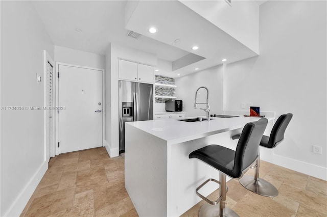 kitchen with white cabinetry, sink, kitchen peninsula, stainless steel fridge, and a breakfast bar area