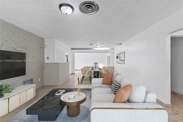 living room featuring light tile patterned flooring, a textured ceiling, and brick wall