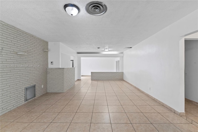 empty room with a fireplace, light tile patterned floors, a textured ceiling, and brick wall