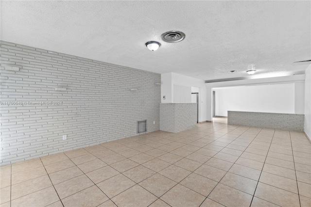 unfurnished living room with light tile patterned floors, a textured ceiling, and brick wall