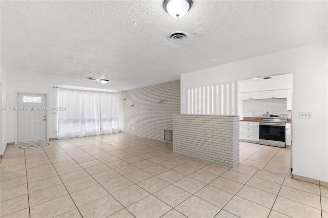 unfurnished living room with light tile patterned floors, a textured ceiling, and brick wall