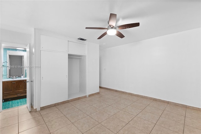 unfurnished bedroom featuring ceiling fan, light tile patterned flooring, ensuite bathroom, and a closet