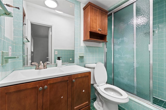 bathroom featuring vanity, a shower with door, tile patterned floors, toilet, and tile walls