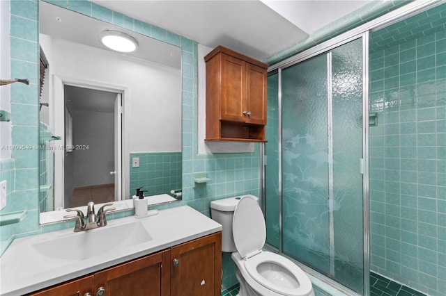 bathroom featuring vanity, toilet, tile walls, and a shower with shower door