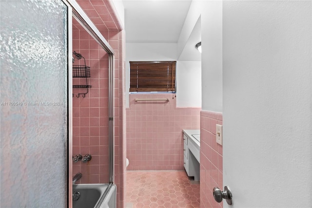 bathroom featuring tile patterned flooring, vanity, bath / shower combo with glass door, and tile walls