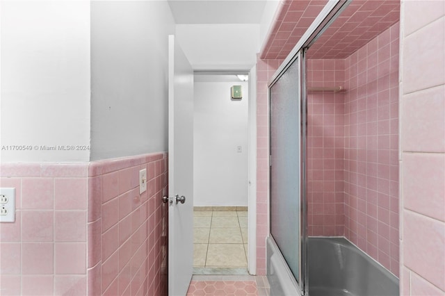 bathroom with tile patterned flooring, tile walls, and bath / shower combo with glass door