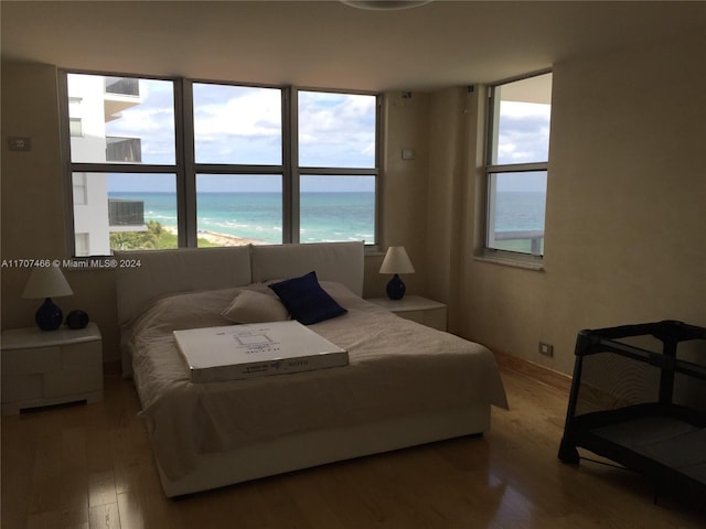 bedroom with hardwood / wood-style floors, a water view, and a beach view