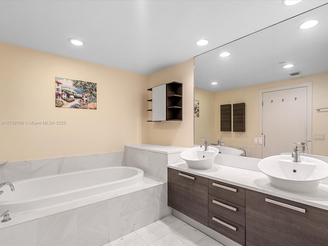 bathroom featuring a relaxing tiled tub and vanity