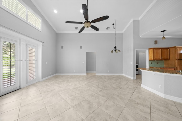 unfurnished living room with light tile patterned floors, crown molding, ceiling fan with notable chandelier, and a high ceiling