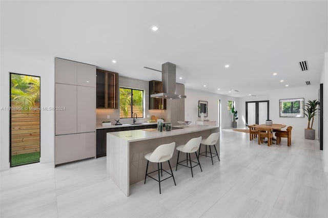 kitchen featuring sink, ventilation hood, a breakfast bar area, a kitchen island with sink, and light tile patterned floors