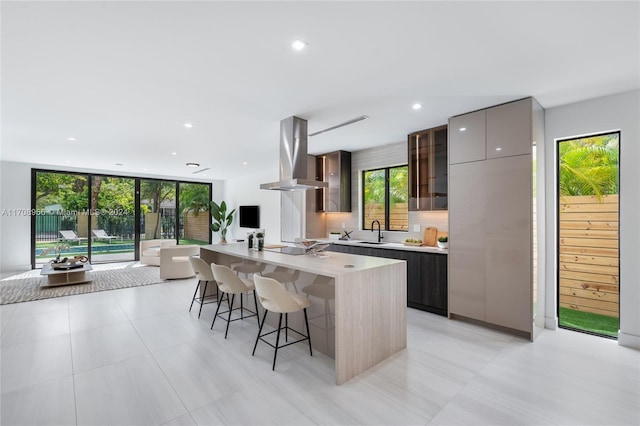 kitchen with a breakfast bar, a kitchen island, wall chimney range hood, and sink