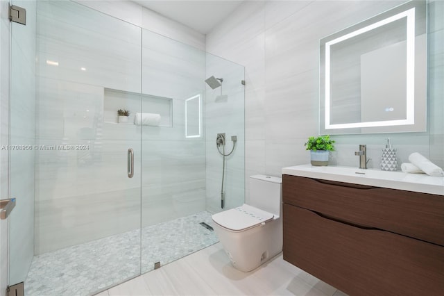 bathroom with tile patterned floors, vanity, a shower with door, tile walls, and toilet