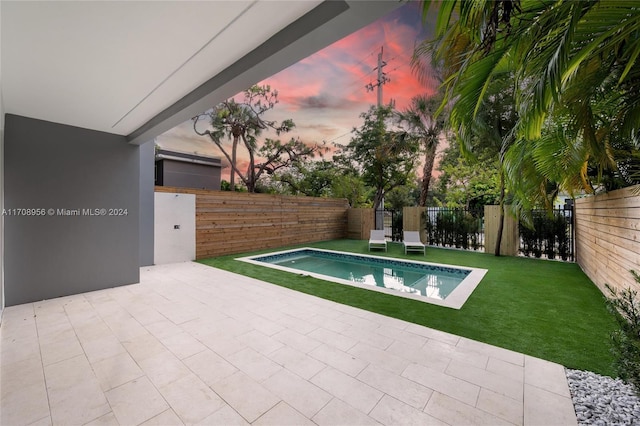 pool at dusk with a patio area and a yard