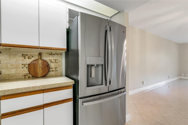 kitchen featuring white cabinets, decorative backsplash, stainless steel fridge, light tile patterned floors, and light stone counters