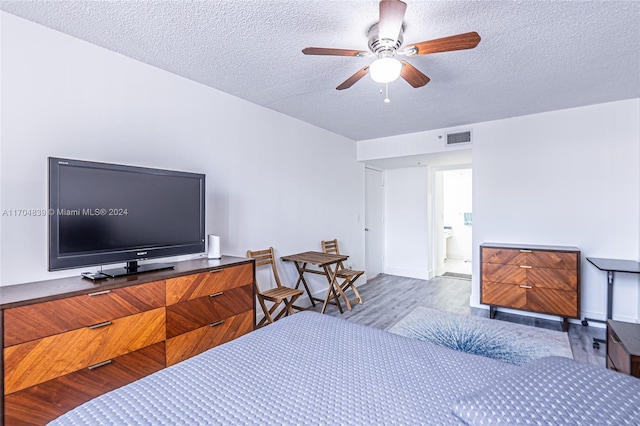 bedroom with wood-type flooring, a textured ceiling, ensuite bath, and ceiling fan