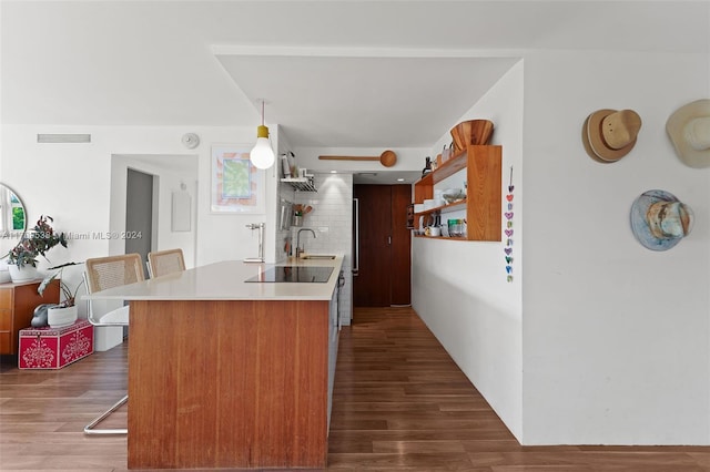 kitchen with sink, hanging light fixtures, a kitchen breakfast bar, dark hardwood / wood-style flooring, and black electric stovetop