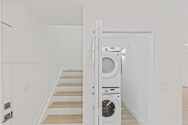 clothes washing area with light hardwood / wood-style floors and stacked washer / drying machine