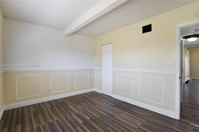 unfurnished room with beam ceiling, a textured ceiling, and dark hardwood / wood-style floors