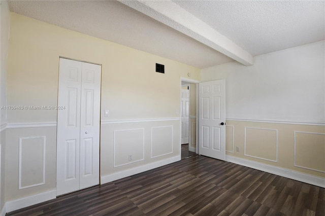 unfurnished bedroom featuring beam ceiling, a closet, and dark wood-type flooring