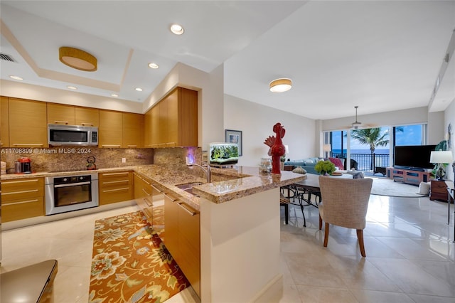 kitchen featuring kitchen peninsula, light stone countertops, backsplash, stainless steel appliances, and light tile patterned flooring