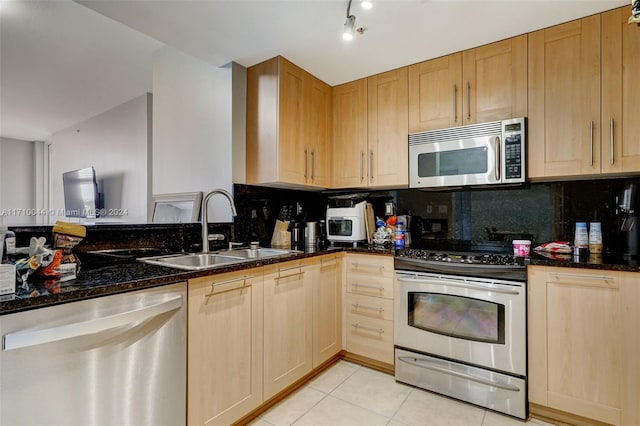 kitchen featuring backsplash, sink, dark stone countertops, light tile patterned floors, and appliances with stainless steel finishes