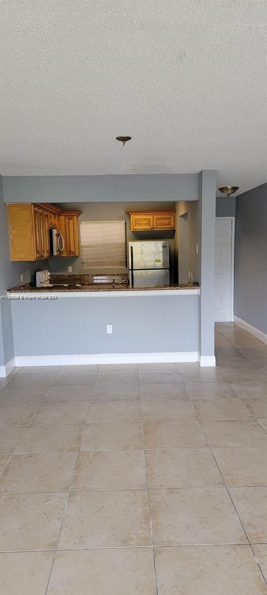 kitchen featuring kitchen peninsula, light tile patterned floors, a textured ceiling, and appliances with stainless steel finishes