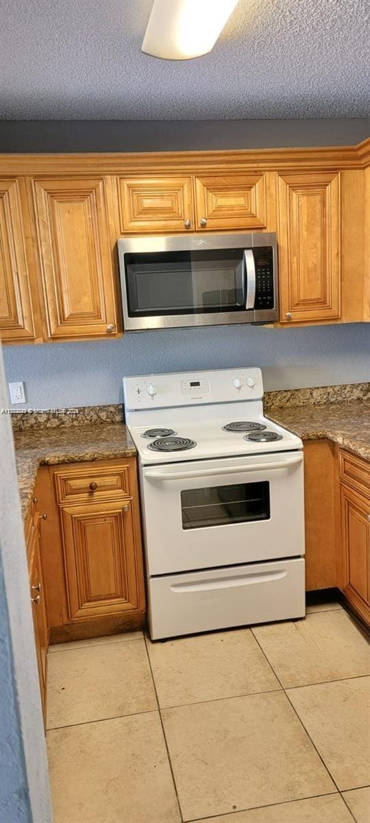 kitchen with light tile patterned floors, white electric range, a textured ceiling, and dark stone counters