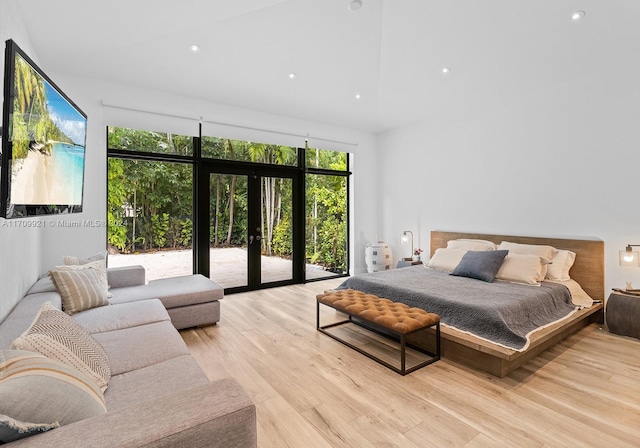 bedroom featuring light hardwood / wood-style floors, a towering ceiling, access to outside, and french doors