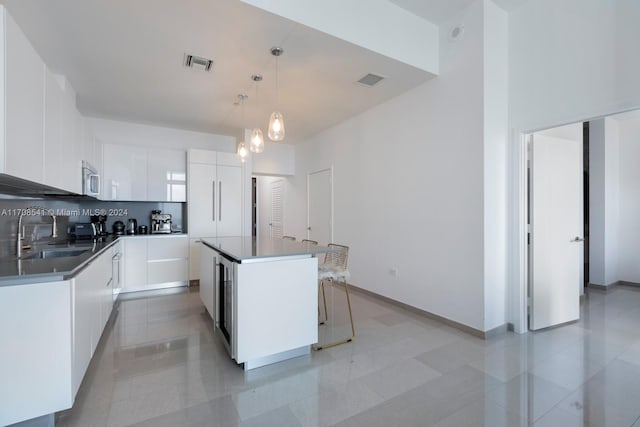 kitchen featuring pendant lighting, a center island, sink, decorative backsplash, and white cabinetry