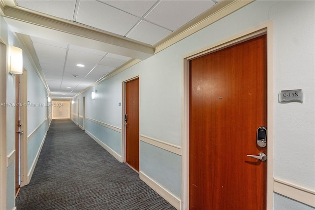 hallway with a paneled ceiling, dark carpet, and ornamental molding