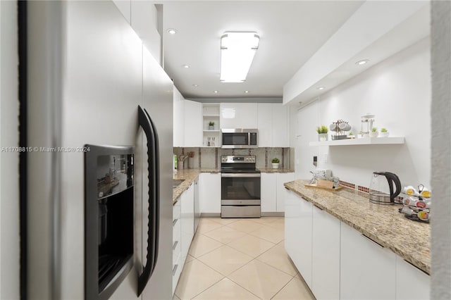 kitchen featuring light tile patterned floors, light stone countertops, white cabinetry, and appliances with stainless steel finishes