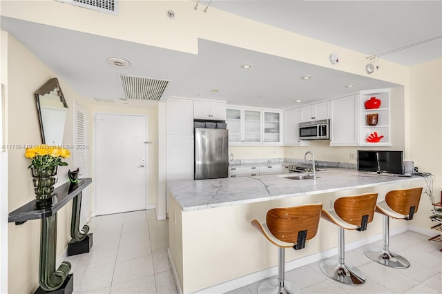 kitchen with kitchen peninsula, appliances with stainless steel finishes, a kitchen breakfast bar, sink, and white cabinetry