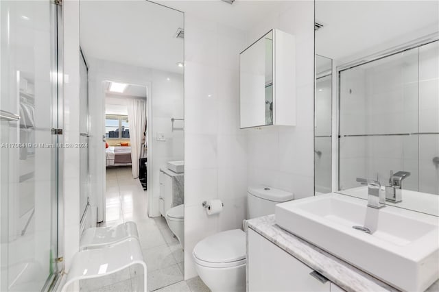 bathroom featuring vanity, a shower with door, tile patterned floors, toilet, and tile walls