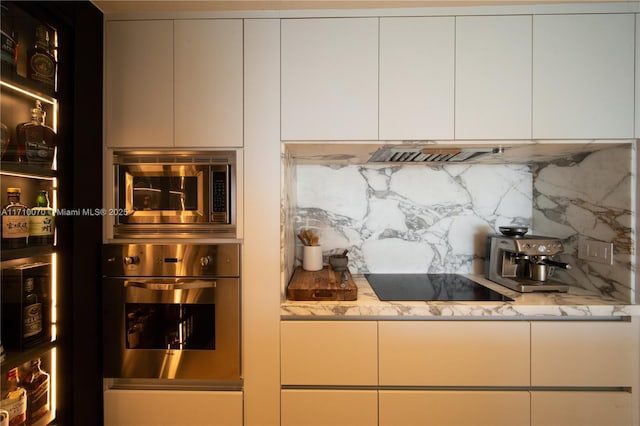 kitchen with white cabinetry, stainless steel appliances, light stone counters, and backsplash