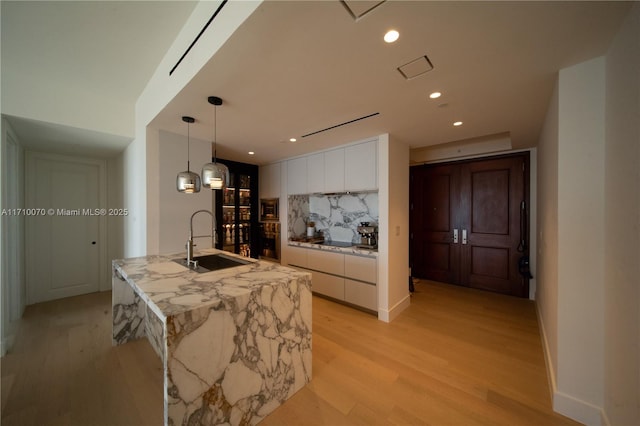 kitchen with decorative light fixtures, an island with sink, sink, white cabinets, and light hardwood / wood-style flooring