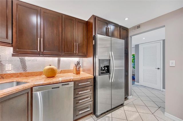 kitchen with tasteful backsplash, light stone counters, dark brown cabinetry, stainless steel appliances, and light tile patterned floors