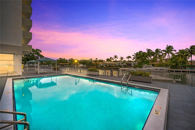 pool at dusk featuring a community pool, fence, a patio, and a gazebo