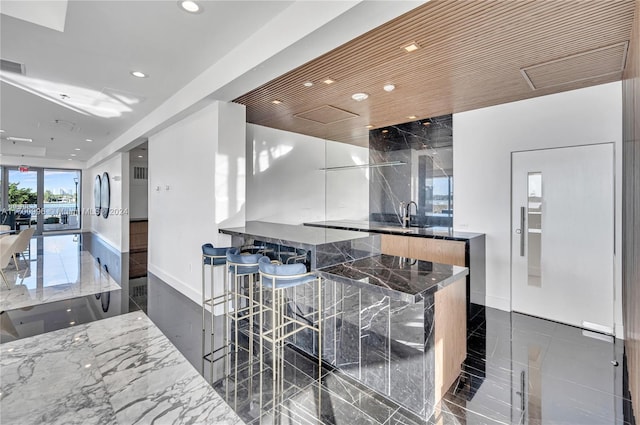 kitchen featuring dark stone countertops, a kitchen bar, white cabinetry, and sink