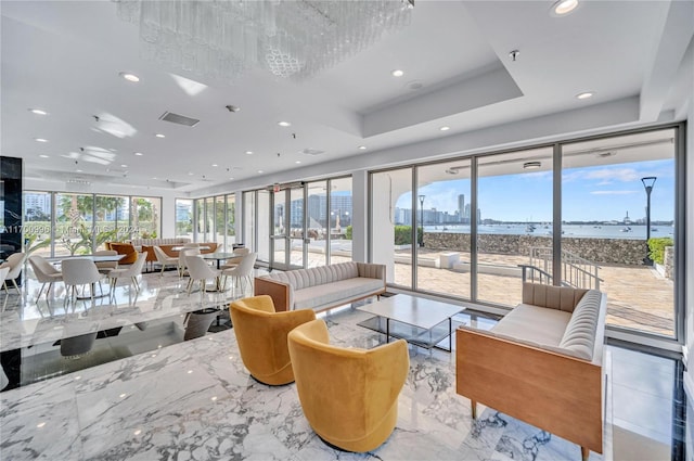 living room featuring a tray ceiling, plenty of natural light, and a water view